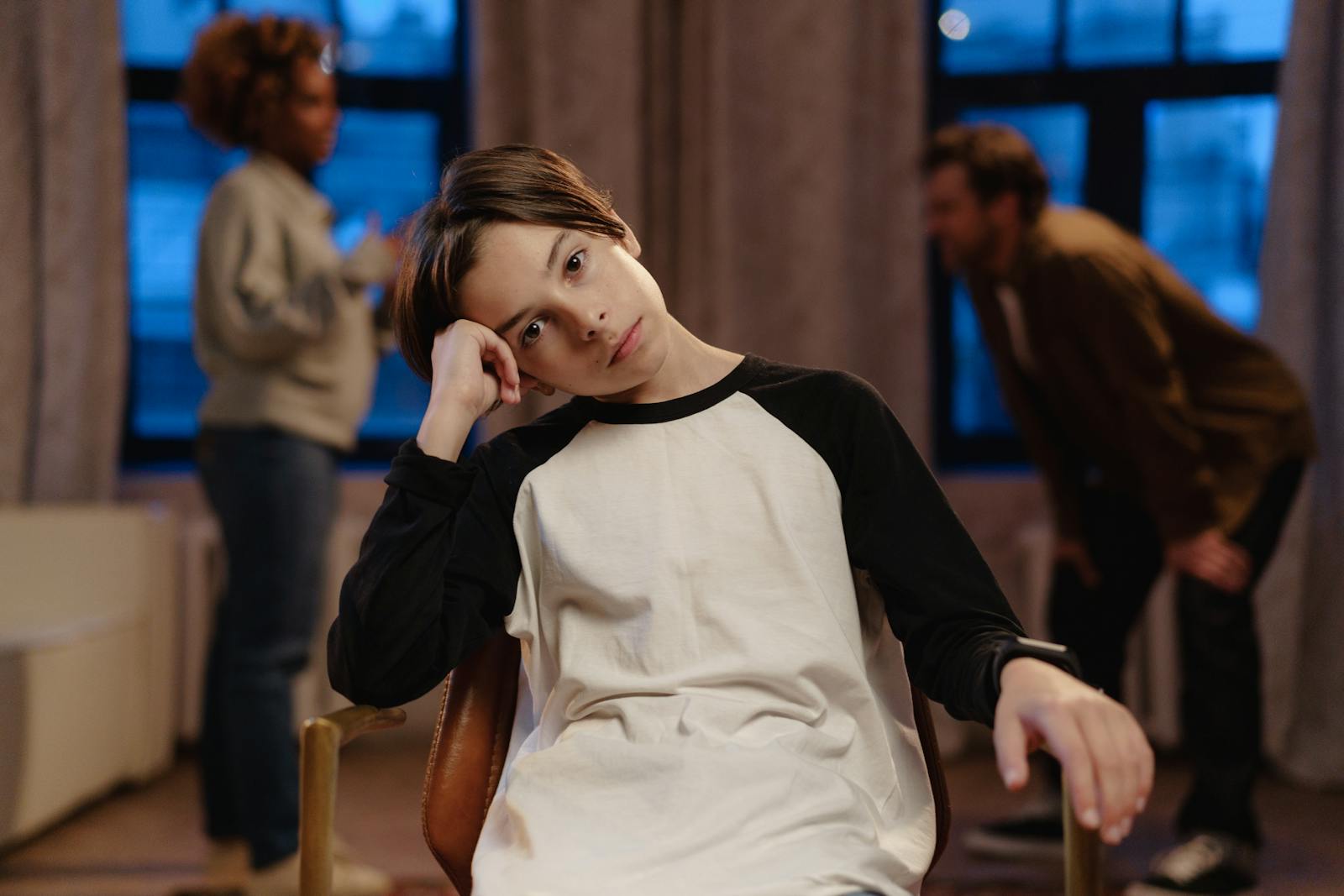 Photo by cottonbro studio A young boy in a black and white shirt looks sad as his parents argue in the background.